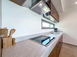 A modern kitchen with a built-in stove, a sink, and wooden utensils on the counter. - 1BR w/Rooftop Pool Downtown (Isla Mujeres)
