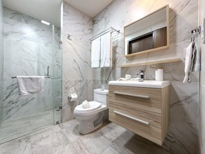 Un baño moderno con cabina de ducha de vidrio, inodoro, tocador con cajones y espejo sobre el lavabo.