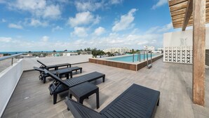 A rooftop terrace with lounge chairs, a pool, and a view of the ocean and buildings. - 1BR w/Rooftop Pool Downtown (Isla Mujeres)