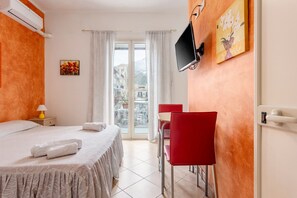 Habitación de hotel con una cama, un escritorio con silla, un televisor y una ventana con cortinas.