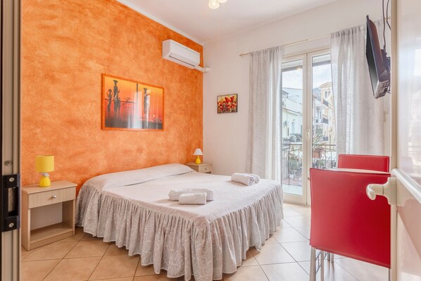 A bedroom with a bed, a nightstand, a red chair, a window with curtains, and a painting on the wall.