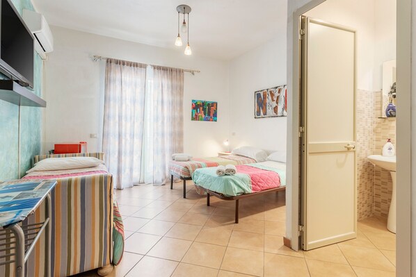 A hotel room with two beds, a television, a bathroom with a sink, and a window with curtains.