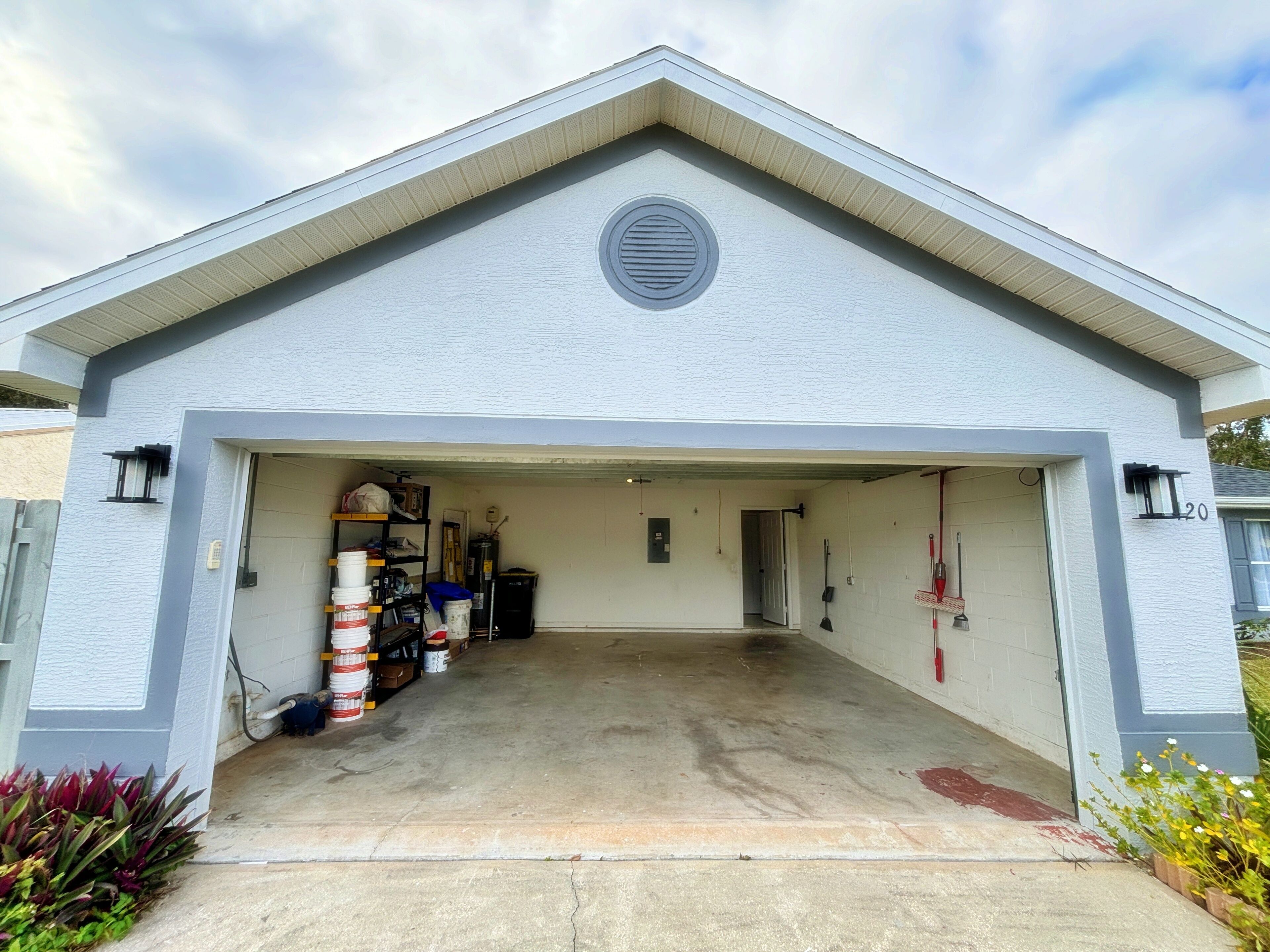A garage with a white exterior, a peaked roof, and a circular vent on the wall.