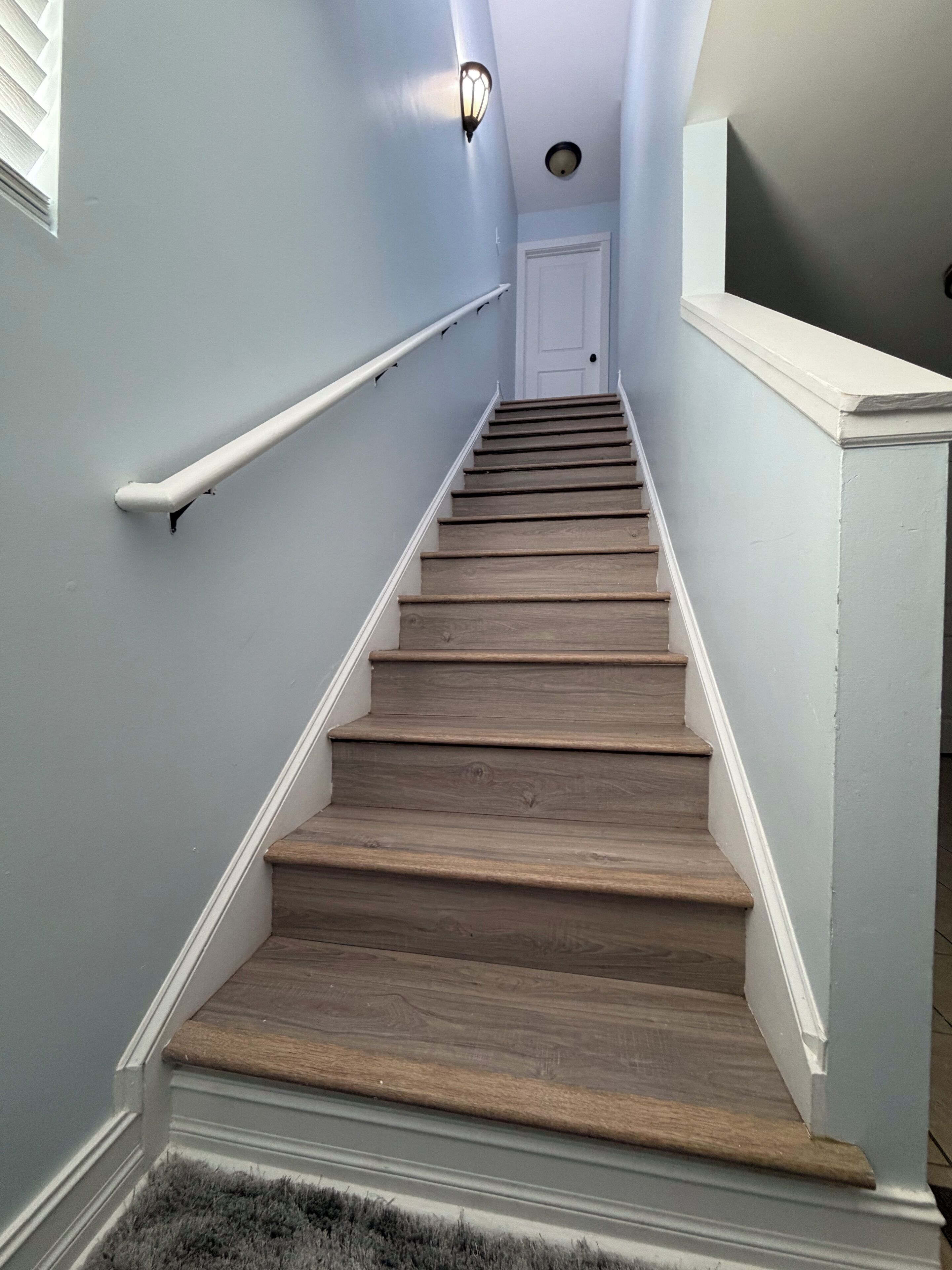 Eine Treppe mit Holzboden und weißen Geländern, die zu einer Tür oben führt.