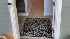 A hallway with a patterned rug, a staircase, and a door leading to a room.