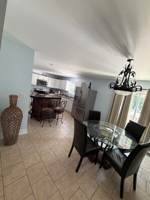 A modern kitchen with white cabinets, a dining area with a glass table, and a decorative vase. - House with JACUZZI * Luxury * 3BR. { ExclusiveDiscounts } (Charlotte)