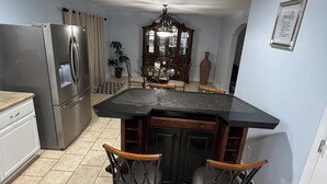A kitchen with a central island, two bar stools, a refrigerator, and a dining table with chairs.
