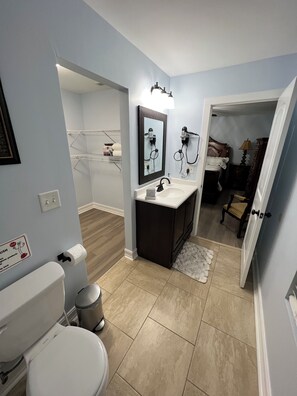 A bathroom with a toilet, sink, and mirror. There is a shower area visible in the background. - House with JACUZZI * Luxury * 3BR. { ExclusiveDiscounts } (Charlotte)