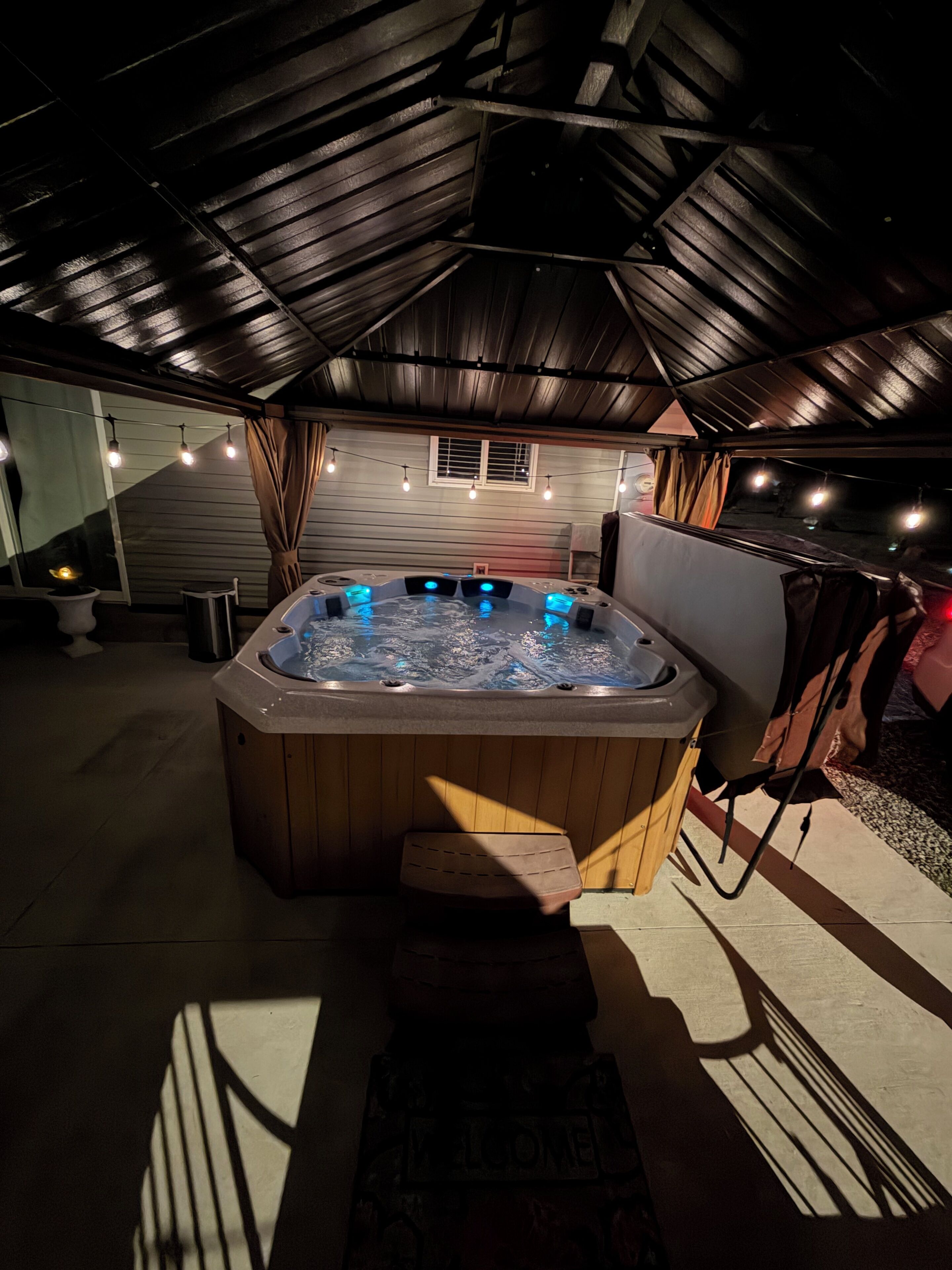 A hot tub in a covered outdoor area with a sloped ceiling and string lights.