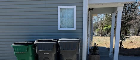Tres botes de basura frente a una casa con porche.