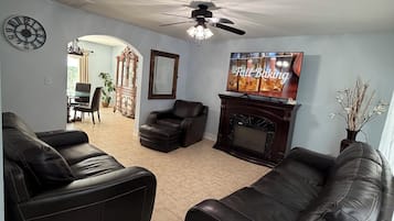 Un salon avec deux canapés en cuir, une cheminée, un ventilateur de plafond et, au fond, un coin repas.