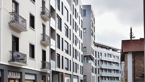 A modern multi-story building with balconies, a visible storefront with signage, and a clear sky. - Muinoa 2 by FeelFree Rentals (San Sebastián)