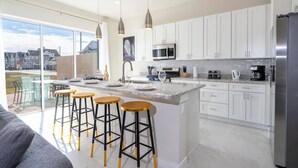 Una cocina moderna con armarios blancos, una isla grande con taburetes, electrodomésticos de acero inoxidable y vistas al vecindario.