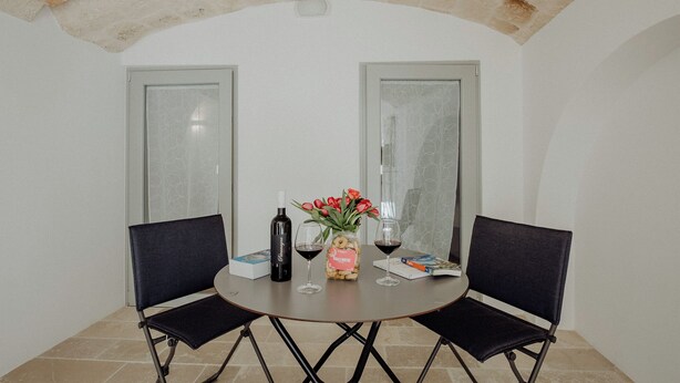 A small round table with two chairs, a bottle of wine, two wine glasses, a vase with flowers, and a box of chocolates. - Hidden House by Monholiday (Monopoli)