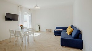 A modern living room with a white dining table, blue sofa, and a TV mounted on the wall. - Rainbow Relax Home by MONHOLIDAY (Monopoli)