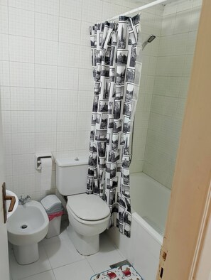 Un baño con inodoro, bidé y cortina de ducha con diseño de paisaje urbano.
