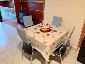 Un comedor con una mesa cubierta por un mantel estampado con motivos de frutas, rodeado por cuatro sillas.