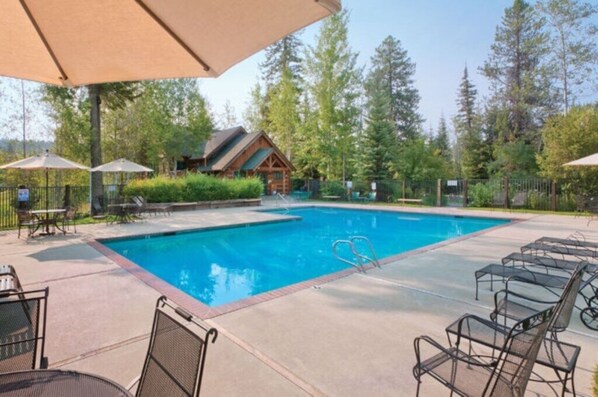 Relax by the serene pool surrounded by lush greenery and tall trees, with lounge chairs and umbrellas providing shaded seating.