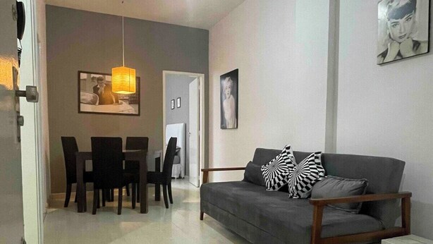 A modern living room with a grey sofa, black and white patterned pillows, a dining table with chairs, and a hanging pendant light. - SUH Copacabana 46 Classy Rio (Rio de Janeiro)