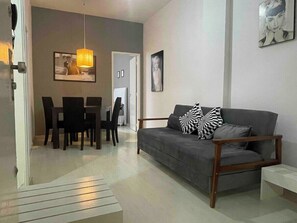 A modern living room with a grey sofa, black and white patterned pillows, a dining table with chairs, and a hanging pendant light. - SUH Copacabana 46 Classy Rio (Rio de Janeiro)