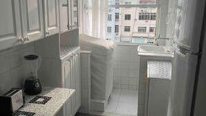 A compact kitchen with white cabinets, a countertop with a patterned tile backsplash, a refrigerator, and a window with curtains. - SUH Copacabana 46 Classy Rio (Rio de Janeiro)
