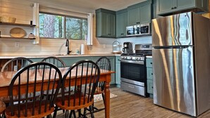 Une cuisine avec des armoires de couleur turquoise, un réfrigérateur en acier inoxydable, un four à micro-ondes, une cuisinière et une table à manger avec des chaises.