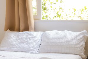 Una cama con ropa blanca y una ventana con cortinas color beige.