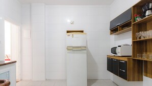 A compact kitchen with a white refrigerator, a microwave, and a wooden shelf with glasses. - SUH Leme 01 Beach Spacious (Rio de Janeiro)