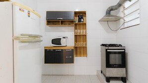 A compact kitchen with a refrigerator, microwave, wooden cabinets, a gas stove, and a built-in shelf with glasses. - SUH Leme 01 Beach Spacious (Rio de Janeiro)