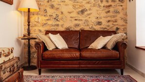 Ein braunes Ledersofa mit weißen Kissen, einer Lampe und alten Koffern vor einer Steinwand.
