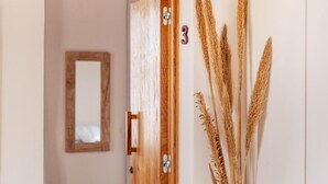 Ein Flur mit einer Holztür, die mit der Nummer 3 gekennzeichnet ist, einem Spiegel an der Wand und einer Vase mit Trockenpflanzen.