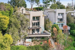 Une maison moderne à plusieurs étages, dotée d’un balcon, d’un jacuzzi et d’un chemin bordé de pierres.