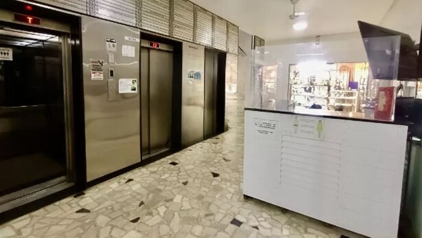 Un corridoio interno con pavimento piastrellato, una reception e tre ascensori.