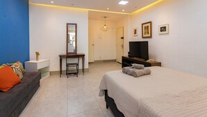 Una camera da letto moderna con un letto, una scrivania, una sedia, una televisione e un bagno visibile attraverso una porta aperta.