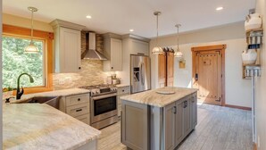 A modern kitchen with a central island, stainless steel appliances, and a stone backsplash. - Luxury 4BR Ski Retreat, Fireplace, Fire Pit, Mtn Views (Thornton)