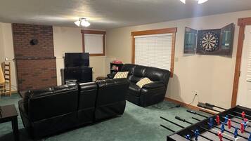 Ein Wohnzimmer mit Ledersofa, Fernseher, Dartscheibe und Kicker.