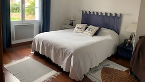 Quarto com cama grande, mesa de cabeceira, janela com cortinas e vista para o verde lá fora.