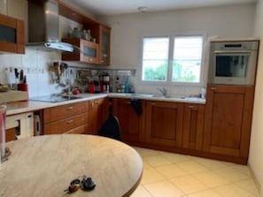 A kitchen with wooden cabinets, a countertop, a stove, and a window. - Charming Pornic House with Blue Shutters, Terrace and Garden (Pornic)