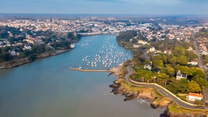 Vista aérea de uma cidade costeira com um porto de iates, casas e uma imponente construção que lembra um castelo.