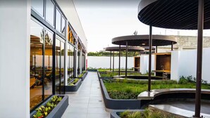 Un bâtiment moderne doté de grandes fenêtres, d’un espace extérieur couvert avec des sièges et d’un chemin bordé de jardinières.