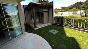 Une terrasse extérieure moderne, dotée d’un barbecue intégré, d’un petit espace salon couvert et d’une pelouse bien entretenue.