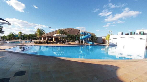Une piscine avec un toboggan, un espace de repos couvert et un bâtiment doté d’un toit en pente.