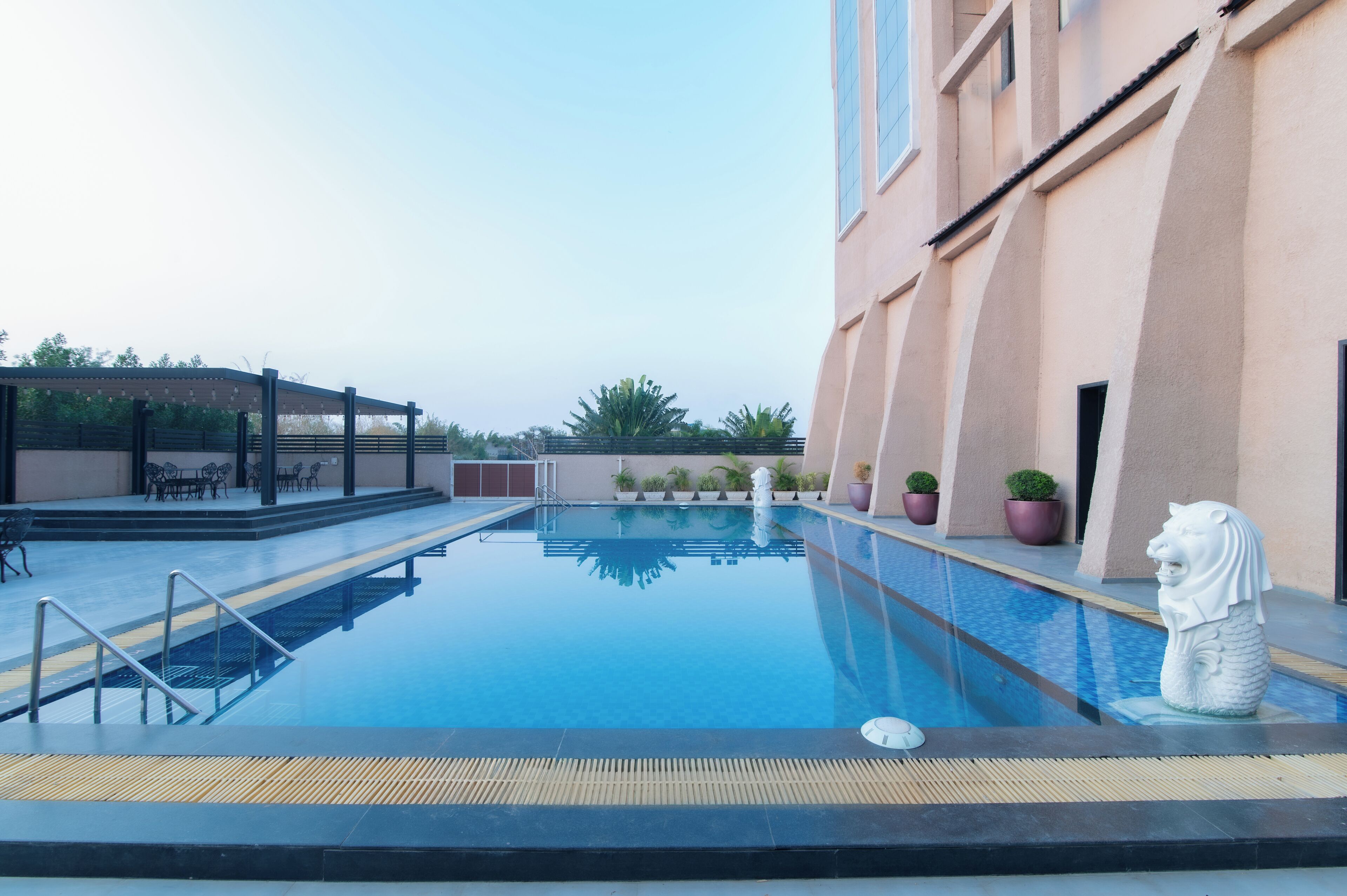 A swimming pool with a statue, outdoor seating, and potted plants.