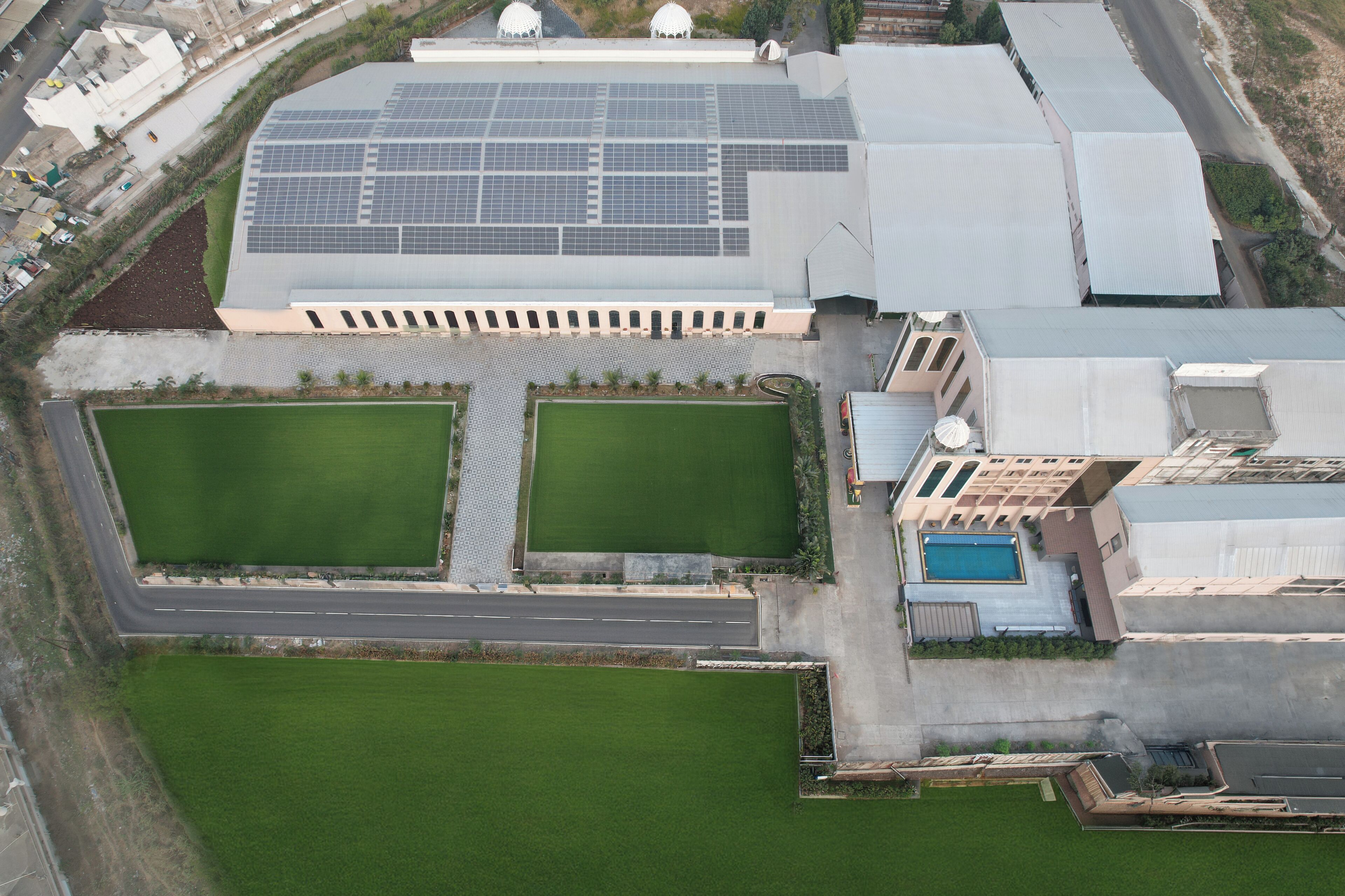 An aerial view of a building with solar panels, two green lawns, and a swimming pool.