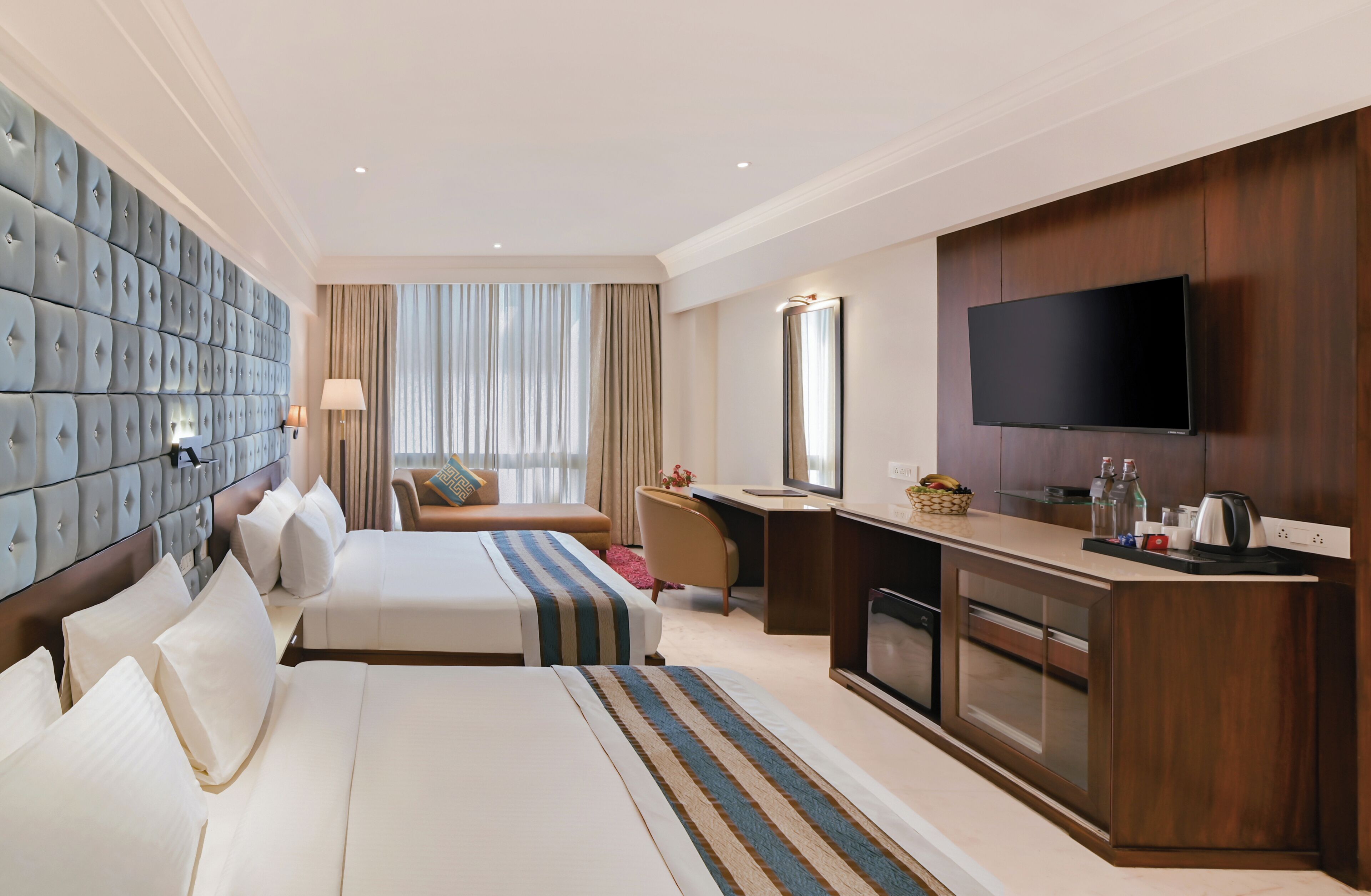 A hotel room with two beds, a desk, a TV, and a minibar.