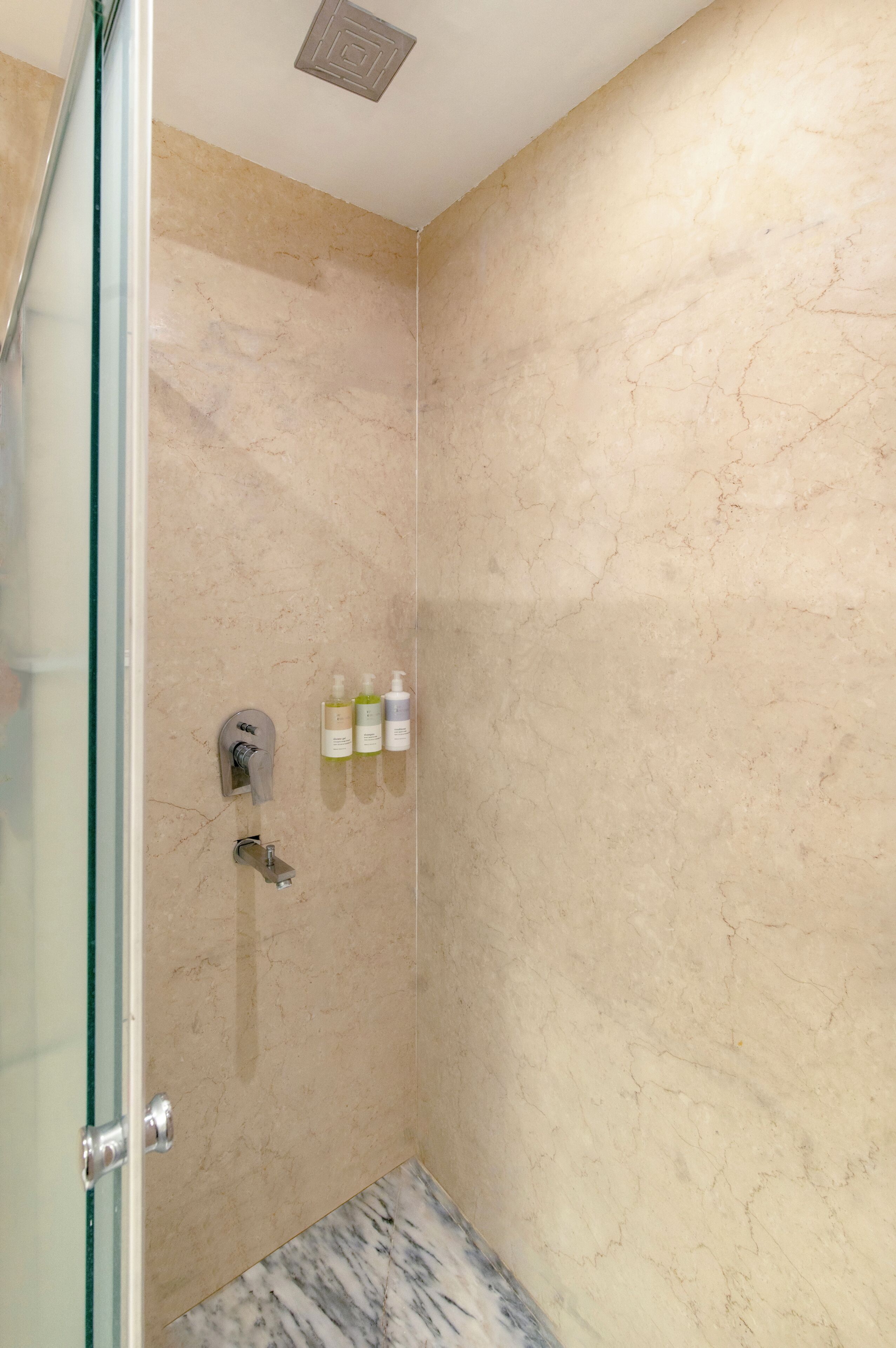 A glass-enclosed shower with a marble wall, a towel rack, and a soap dispenser.