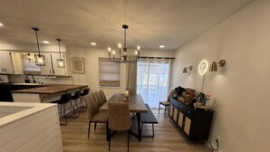A modern kitchen with a dining area, wooden flooring, and pendant lighting.