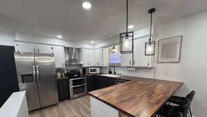 A modern kitchen with stainless steel appliances, a wooden island, and black bar stools.