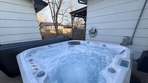 A hot tub with a control panel, surrounded by a wooden deck and a house in the background.