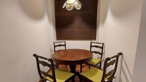 Un comedor con una mesa redonda de madera y cuatro sillas, cada una con un cojín verde. Una lámpara colgante se encuentra sobre la mesa.